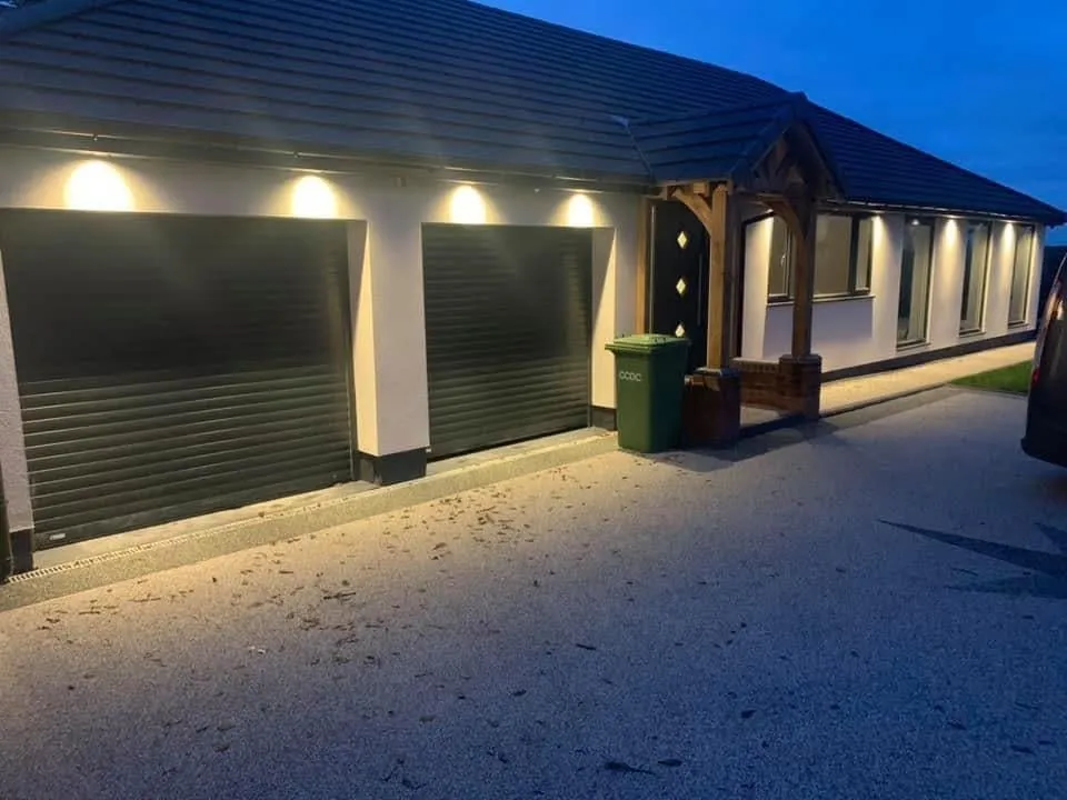 Exterior soffit lighting installed above a garage and entrance, lit at dusk